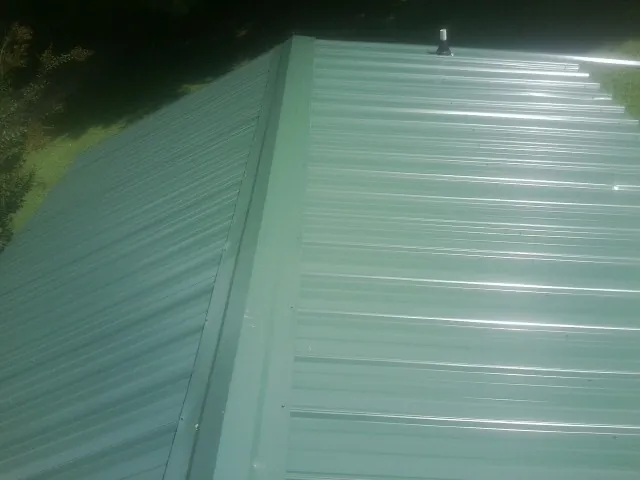 New green metal panels meeting at the ridge of a roof — Flat Roof Repair work by our crew in New Haven